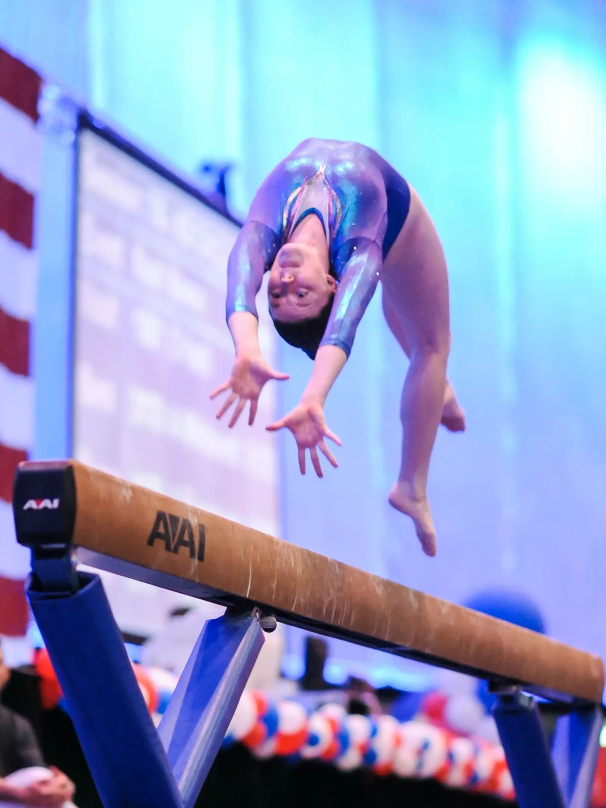Krystina mid-flip on a balance beam at a gymnastics meet